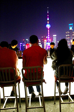 Students sitting at a rooftop bar with the city skyline behind them at night