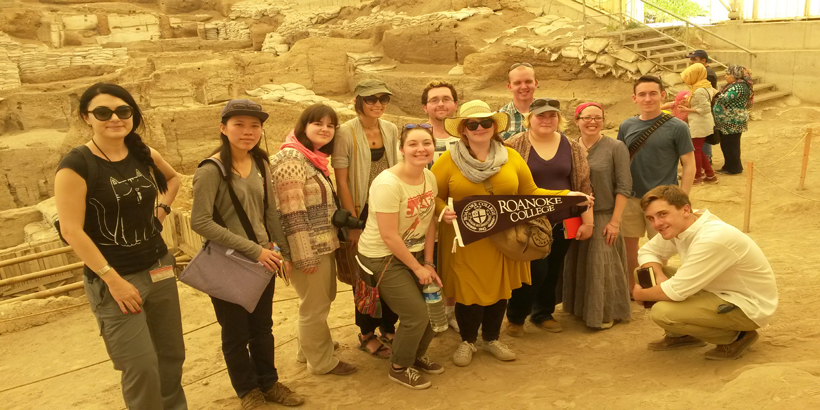 Faculty and students hold a Roanoke pennant flag outside an archeological site