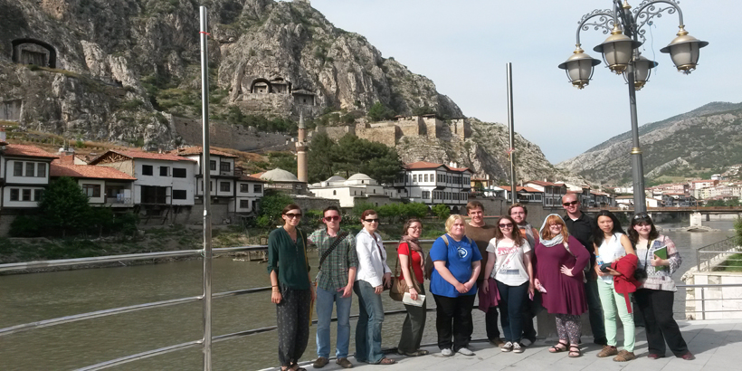 Students and faculty pictured alongside a canal with a view of mountains in the background