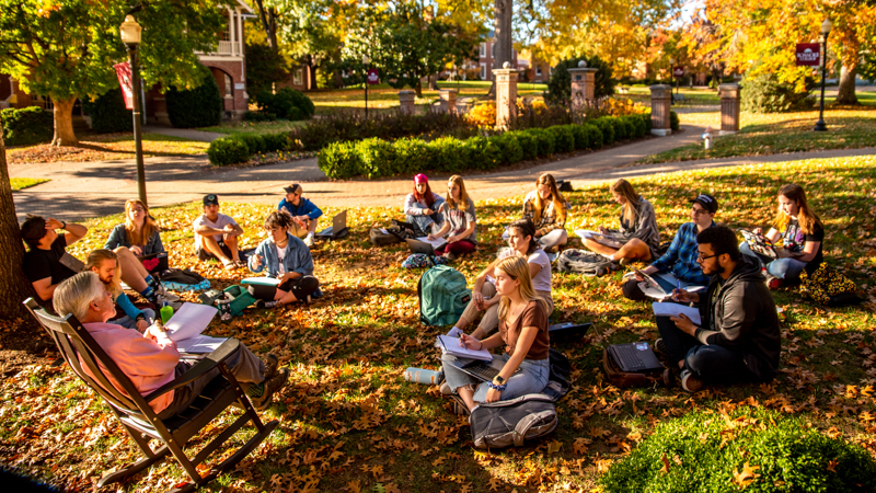 Students enjoying class outside among fall leaves