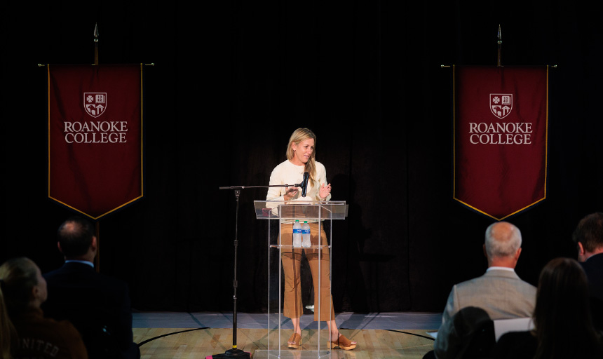 Kristin Armstrong speaks at a lectern flanked by Roanoke College flags