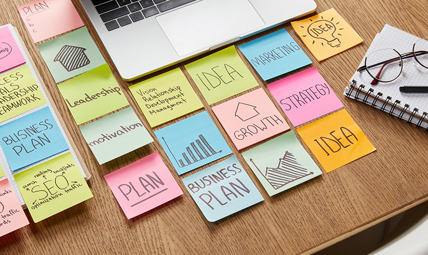 Desk covered with multi-colored sticky notes with words like: Business Plan. Growth. Strategy.