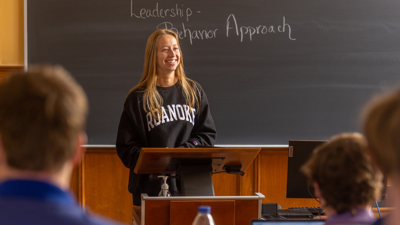 Student in Roanoke sweatshirt smiling while giving a classroom presentation