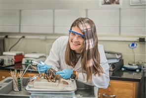 student smiles for a photo while working with lab items