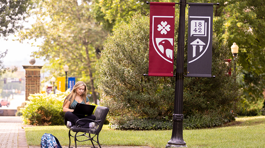 student sitting on bench studying on the front quad