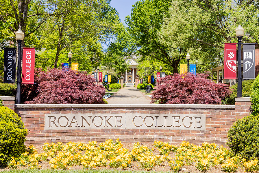 Framed by flowers and banners, an entrance sign greets visitors with the words: Roanoke College