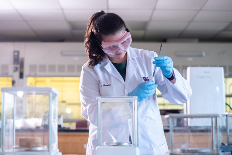 A student researcher dressed in a lab coat prepares a sample for an experiment