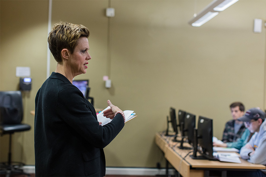 A professor stands at the front of a room while addressing students