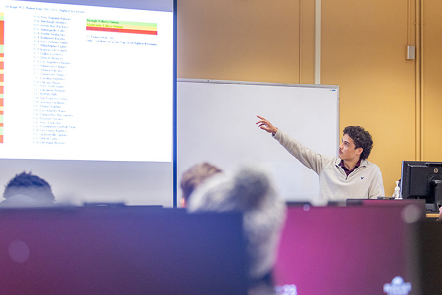 A student explains a data spreadsheet during an ecnomics presentation