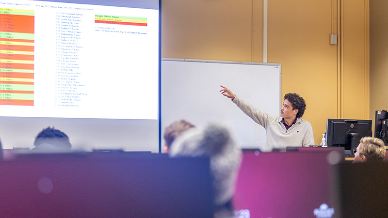 A student explains a data spreadsheet during an ecnomics presentation