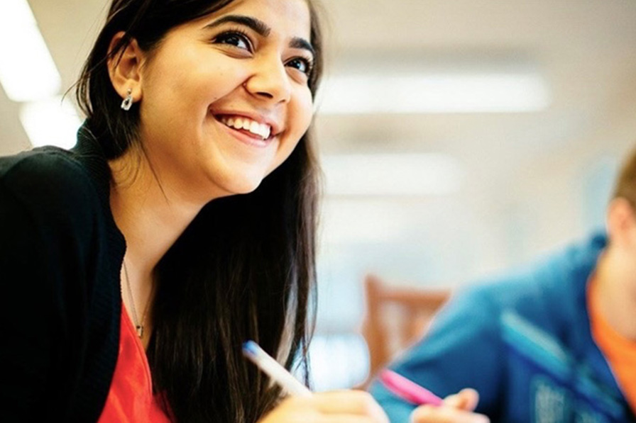 A student studying at a table looks up and smiles