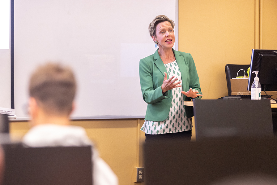 A professor gestures while addressing students from the front of a classroom