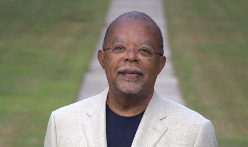 Dr. Henry Louis Gates Jr stands on sidewalk with grass on each side