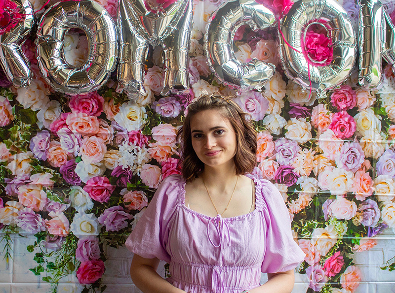 Photo of Joyelle Ronan under a string of letter balloons that spell out ROM COM