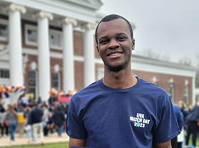 Photo of William Osae at UVA smiling and holding up a sign announcing his medical residency match at Duke 