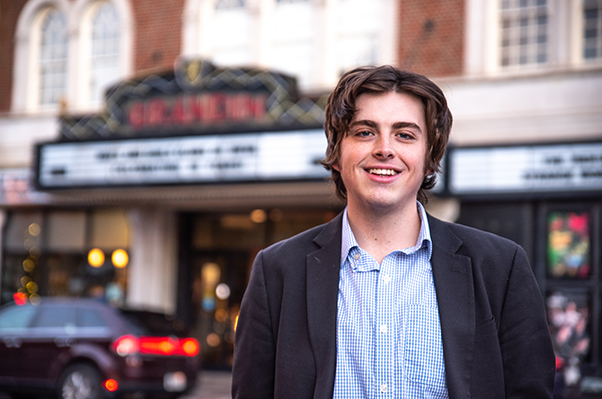 Young man stands in blue shirt and sports coat with Grandin Theatre marquee in the background
