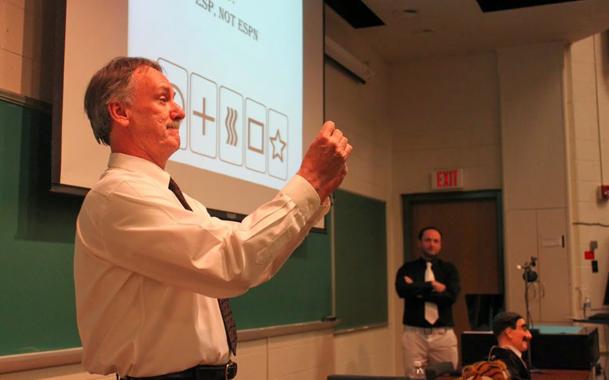 A professor stands at the front of a classroom readying a magic trick