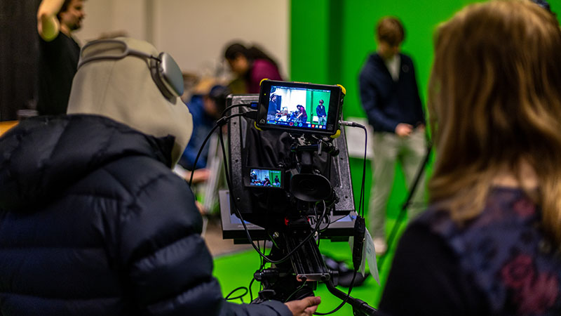 students operate a camera with a green screen in the background