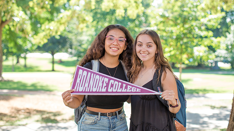 two students holding a Roanoke College pennant