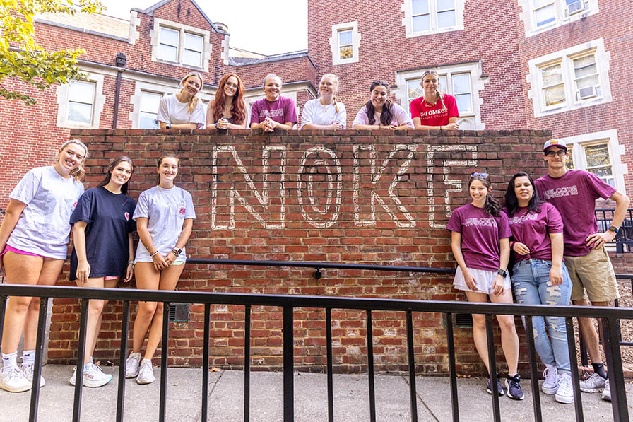 A group of students standing in front of brick wall with NOKE written on it