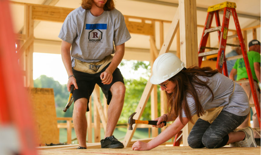 freshman student hammering nail as Habitat volunteer looks on