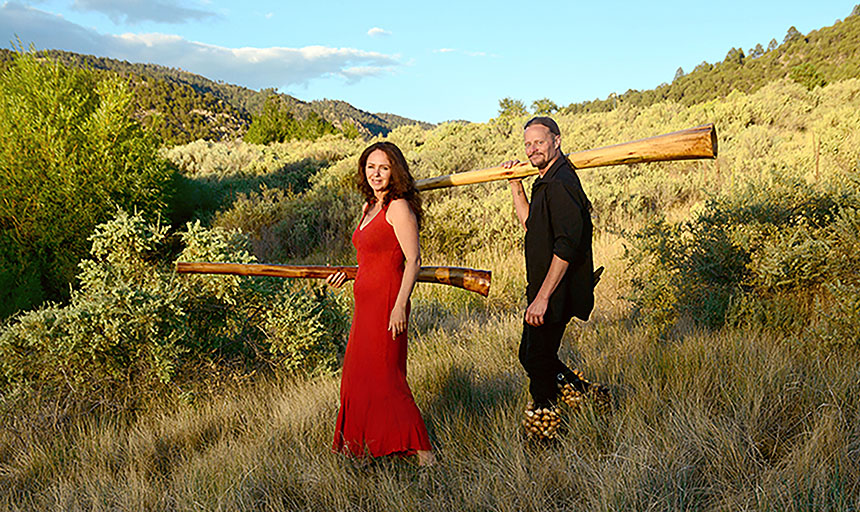 Woman in red dress with man wearing black both holding a wooden instrument.