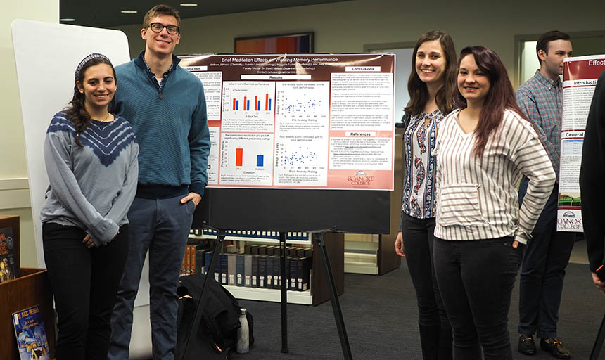 Students gathered around a poster explaining their research