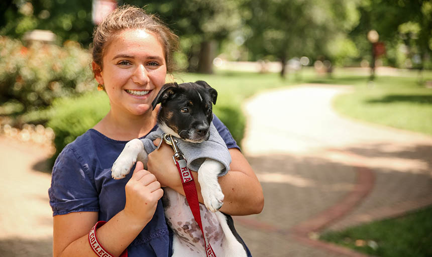 A student holding her puppy and smiling