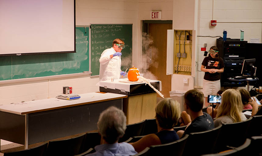 A student standing behind a jack-o-lantern with foam coming out of it