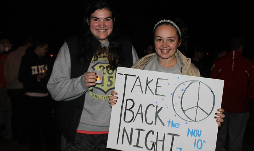 two female students smiling with a sign that says Take Back the Night