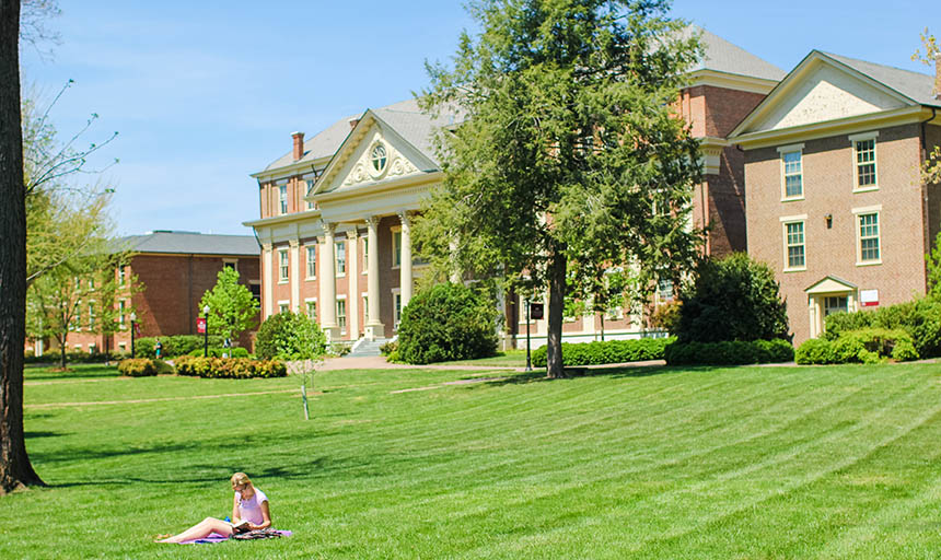 A student sitting on the front quad with the administration building and trout hall behind her