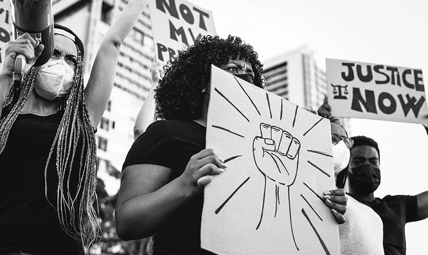 A black and white photo of protesters, one of them is holding a sign with a raised fist