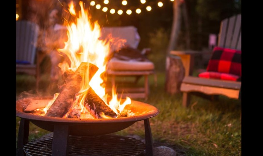 A photo of a bonfire and empty chairs placed beside it