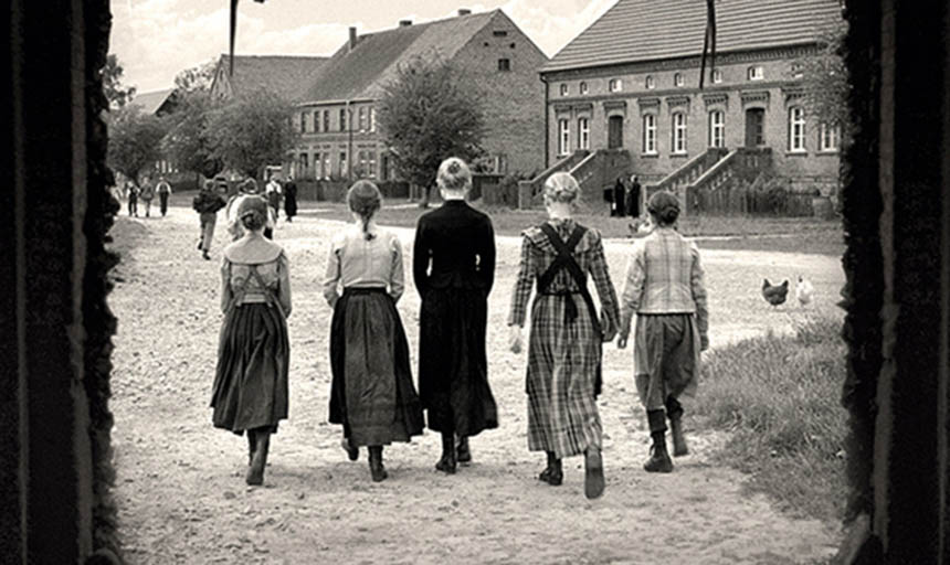 A black and white photo of a behind shot of a group of women walking towards buildings