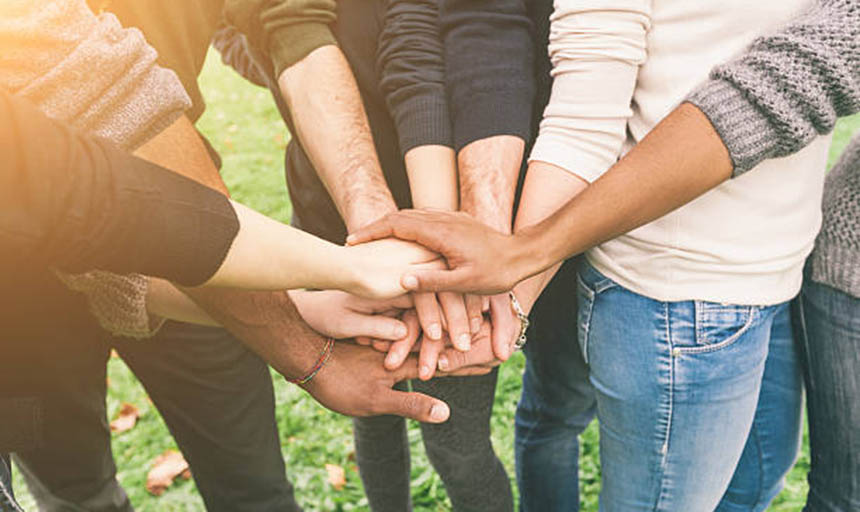 people of various races reaching in and placing their hands on top of each other's in the center of a circle