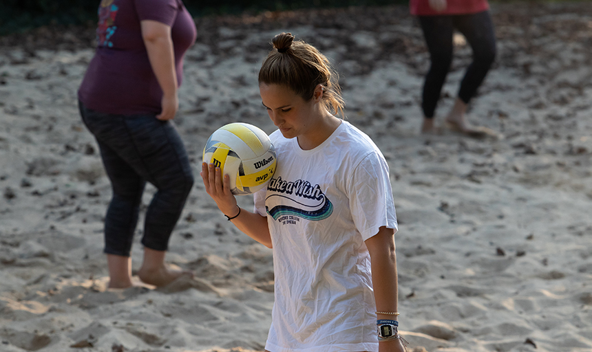 A student holding a volleyball on the volleyball court