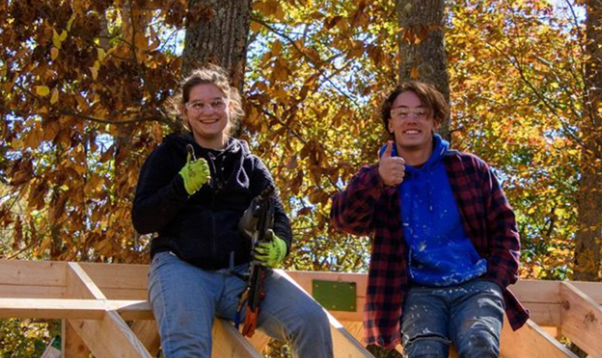 Two students on a prior trip give up a thumbs up while working on a habitat for humanity build