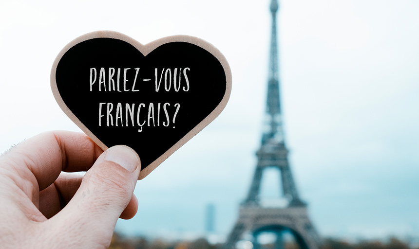 Heart-shaped sign reading, Parlez-Vous Francais, being held up in front of the Eiffel Tower