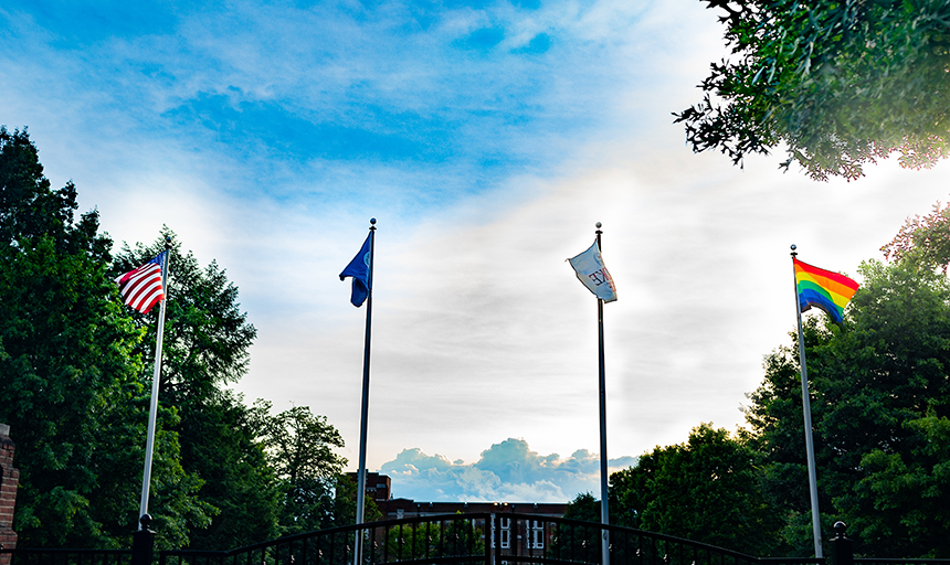 pride flag flying with other flags on the back quad