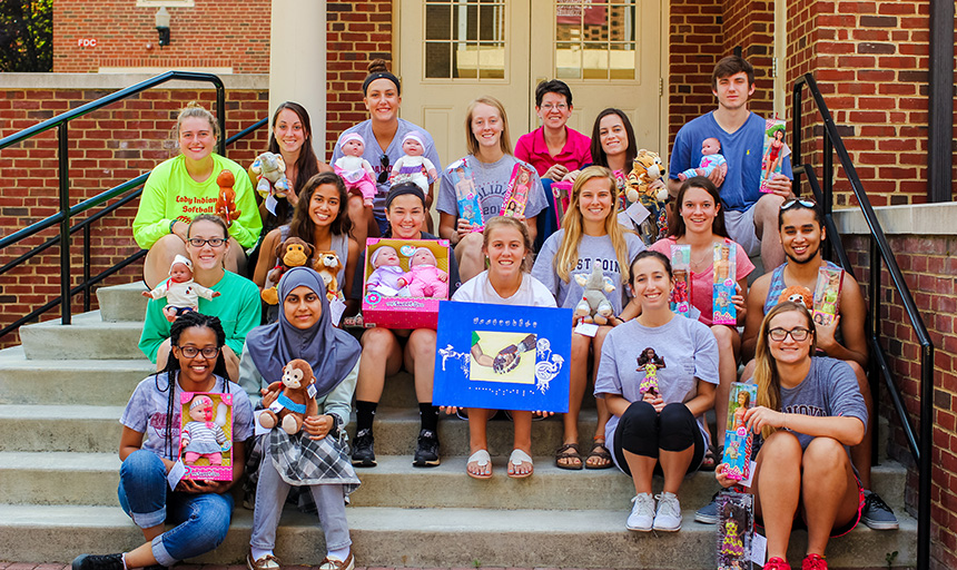 Students smile for a photo while holding up toys that were modified to be representative of children with disabilities