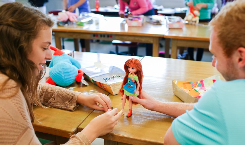 Two students sitting at a table work together to modify a doll