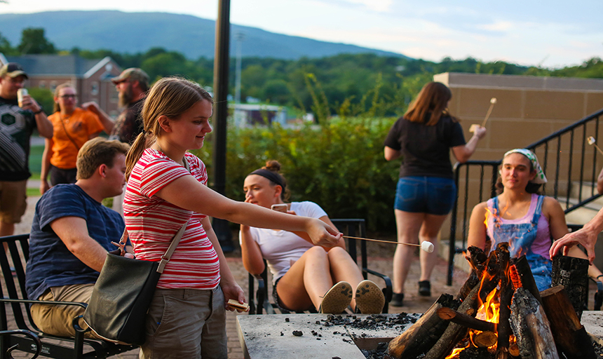 student roasting marshmallow over a fire pit.