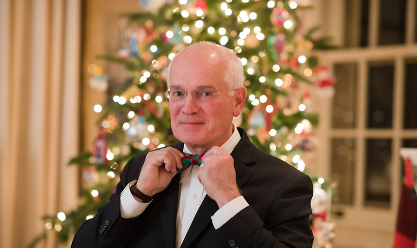 President Maxey ties bow tie in front of Christmas tree