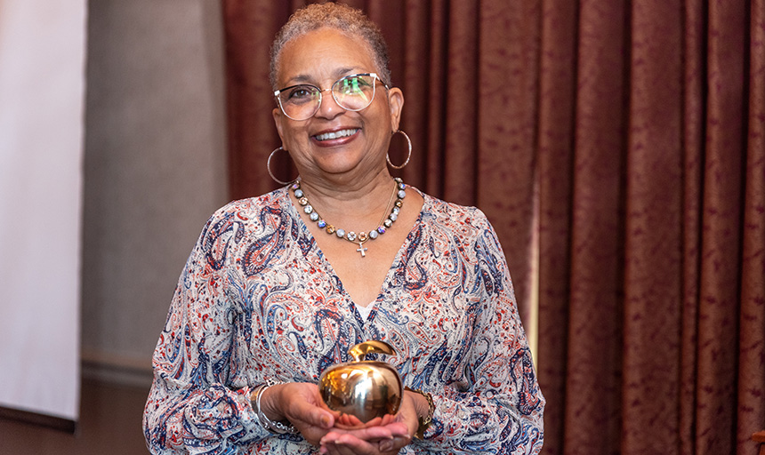 Woman smiles at camera while holding an apple shaped award trophy