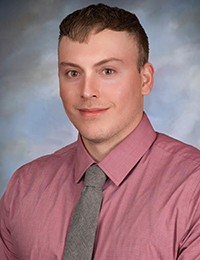 Dylan Jones in a professional headshot wearing a pink shirt and grey tie.