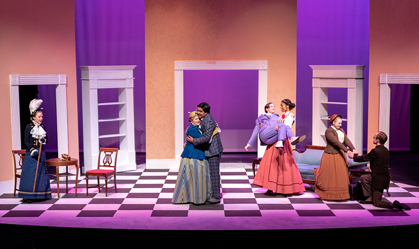 Cast members pose on stage in various embraces during a dress rehearsal