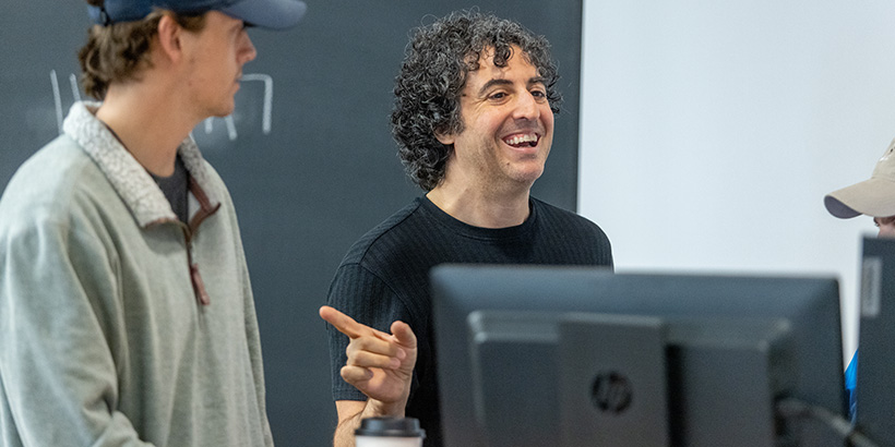 Professor Edward Nik-Khah smiles as he talks with a team of students running an experiment