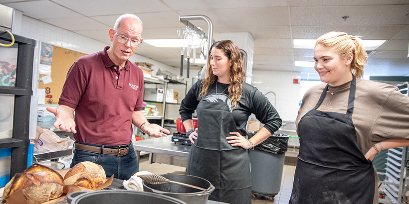 Two students smile as Professor Adkins comments on the fresh bread just baked by their class