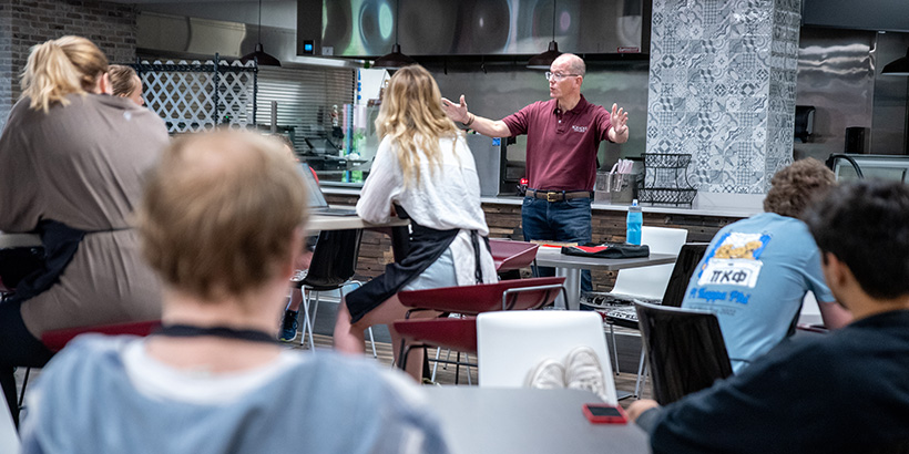 Professor Adkins gestures with his arms outstretched in front of him as he addresses his class