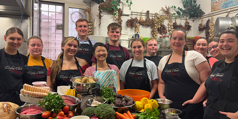 Students smile in a kitchen while surrounded by fresh, colorful produce